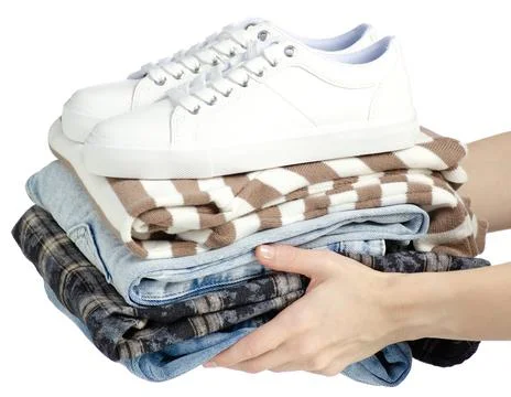 Hand holding stack of clothes jeans with white sneakers Stock Photos