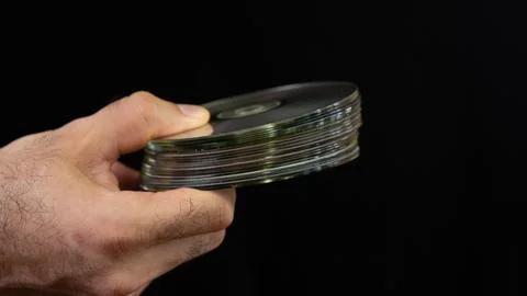 Hand holding a stack of compact discs with a black background, showcasing a.. Stock Photos