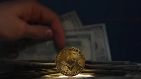 Hand Holding a Stack of Dollar Bills with an Ethereum Coin in Front of a Stock Footage 296566153