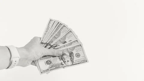 Hand Holding a Stack of Hundred Dollar Bills on Cream Backdrop. Financial Foto stock