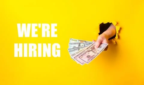 Hand holding a stack of money with the words We're hiring written below it Stock Photos