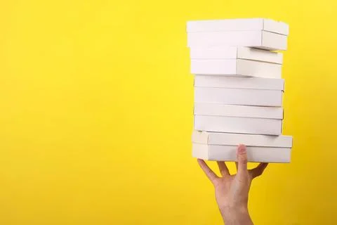 Hand holding a stack of white boxes against yellow background Stock Photos
