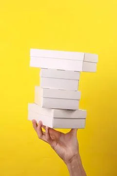 Hand holding stack of white boxes against yellow background Stockfoto's