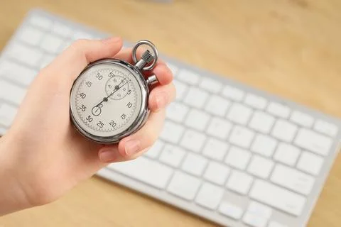 Hand holding stopwatch over computer keyboard Stock Photos