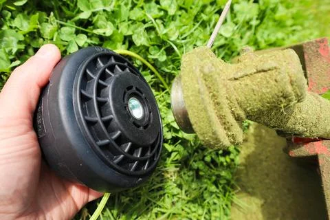 Hand holding string trimmer head replacement next to gearbox shaft Foto stock
