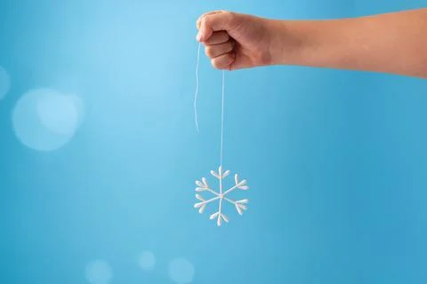 A hand holding a string from which a snowflake-shaped ornament is hanging. .. Stock Photos
