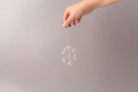A hand holding a string from which a snowflake-shaped ornament is hanging. .. Stock Photos