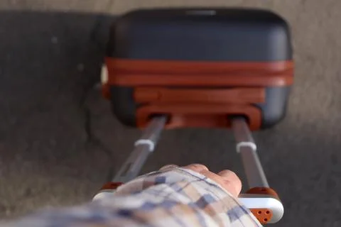 Hand holding suitcase while walking on pavement in an outdoor setting during Stock Photos