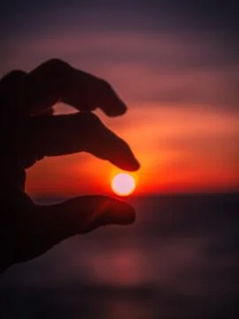 A hand holding a sun setting between the fingers at a seaside Stock Photos
