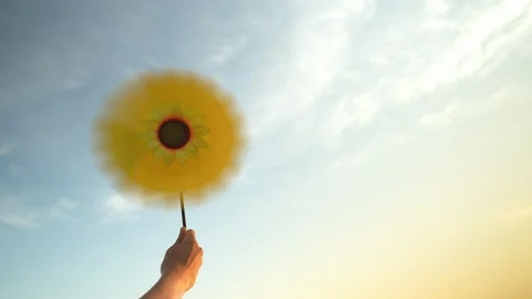 Hand holding a sunflower windmill is rotating speed by the wind with sky Stock Footage 240723895
