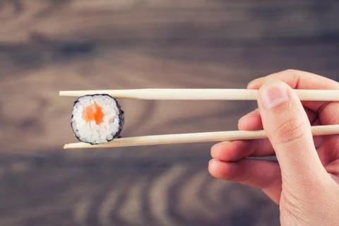 Hand holding sushi roll using chopsticks Stock Photos