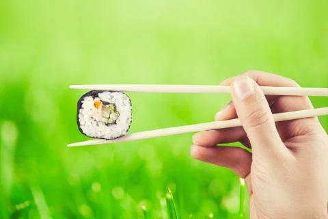 Hand holding sushi roll using chopsticks Stock Photos