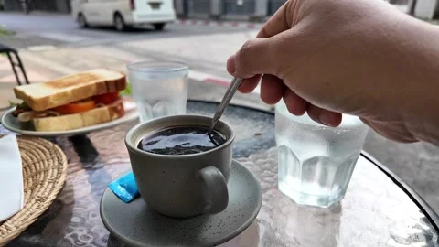 Hand holding tea spoon stirring coffee outdoor at cafe. Stockbeeldmateriaal 277557367