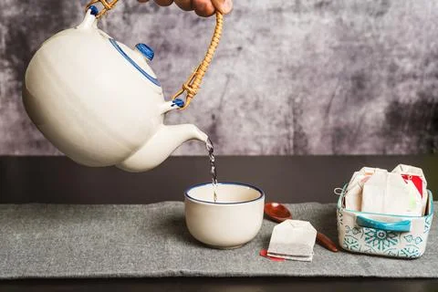 A hand holding a teapot while pouring hot water to prepare the tea, along w.. Stock Photos