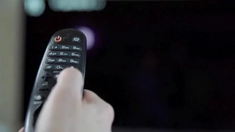 A hand holding the television remote control and is changing tv channels. Stock Footage 257873414