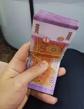 A hand holding a thick stack of two thousand Syrian pound banknotes secured with Stock Photos