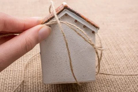 Hand holding a thread around a model house on a brown background Stock Photos
