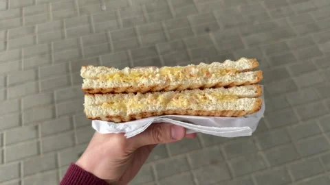 Hand holding toasted egg sandwich cut in half with creamy yellow filling Vídeo Stock 344041461