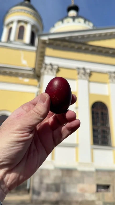 Hand holding a traditional red Easter egg near a church Stock Footage 332736174