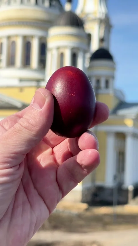 Hand holding a traditional red Easter egg near a church Stock Footage 332736289
