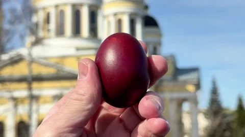 Hand holding a traditional red Easter egg near a church Stock Footage 332736429
