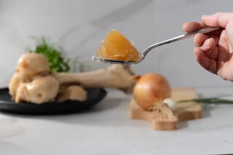 Hand holding triangular orange gel wedge on a spoon in a bright home kitchen Stock Photos