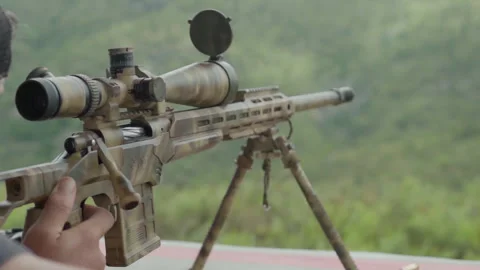A hand holding the trigger of a rifle as a man takes aim, the gun recoils as it Stock Footage 332957337