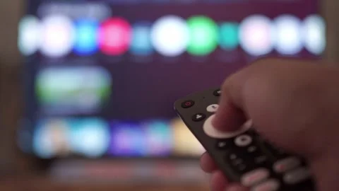 Hand holding TV remote control, browsing streaming apps on blurred smart Stock Footage 342633659