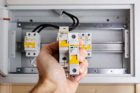 Hand holding two circuit breakers with yellow switches in front of a Stock-Fotos