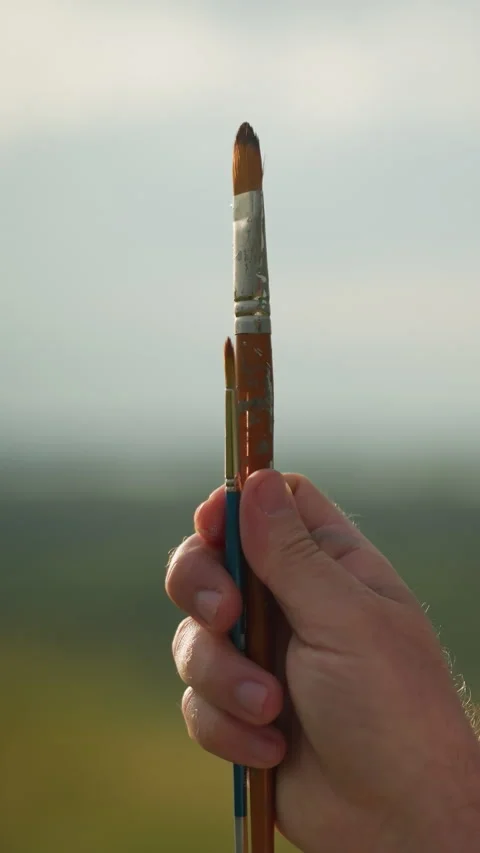 Hand Holding Two Paintbrushes with Face Partially Visible Against Sunny Video stock 306971084