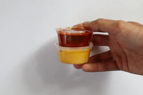 Hand holding two plastic cups with cheddar cheese and chili sauce dip Stock Photos