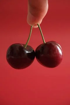 Hand holding two red cherries on red background Stock Photos