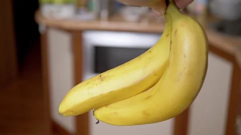 Hand Holding Two Ripe Yellow Bananas in a Blurred Kitchen Environment Video stock 339069235