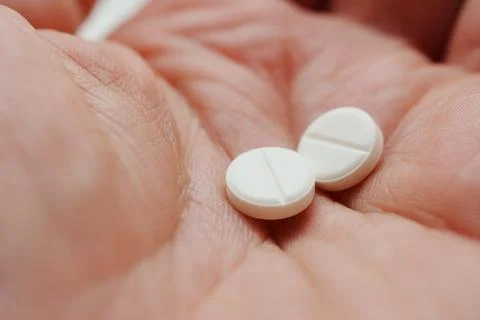 Hand holding two white tablets in close view during daytime Photos