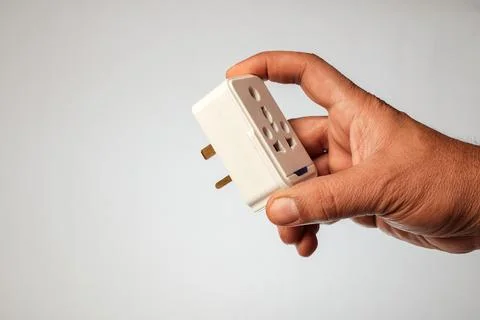 Hand holding a Type G electrical plug adapter with three large rectangular .. Fotos de archivo