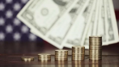 A hand holding US dollar banknotes behind money coins with USA flag Stock Footage 303701203