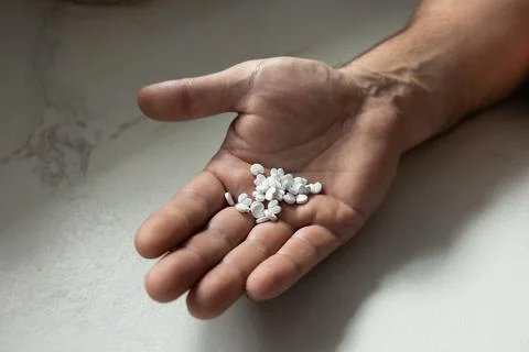 Hand Holding Various Small White Pills on a Light Surface in a Focused Close-Up Stock Photos