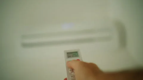 Hand holding a white air conditioner remote controller, pointing towards a Stock Footage 343266394
