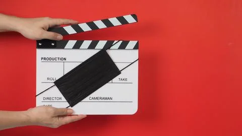 Hand is holding white clapper board with a black face mask on red background. Stock Photos