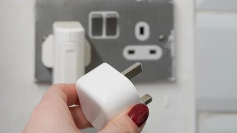 Hand holding white electrical plug near wall socket with copy space Stock Photos
