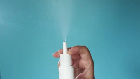 Hand holding white nasal spray bottle, mist spraying against blue background Stock Footage 340264085