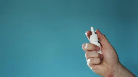 Hand holding a white nasal spray bottle against a blue background Stock Footage 340264622