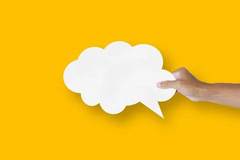Hand holding white paper cloud shape speech bubble balloon isolated on yell.. Stock Photos