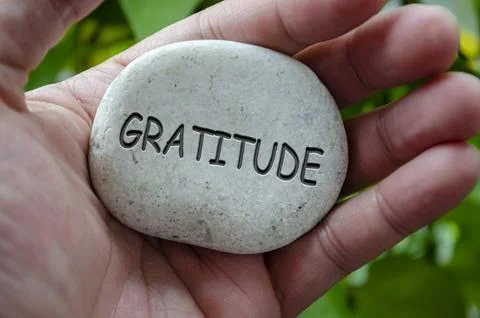 Hand holding a white stone with GRATITUDE text engraved on it, representing.. Stock Photos