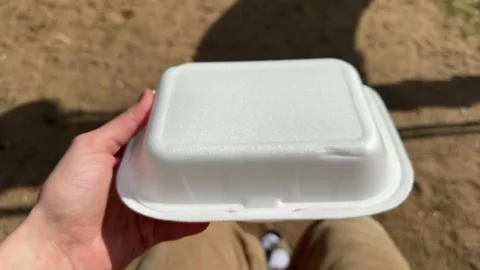 A hand holding a white styrofoam takeout container outdoors on a sunny day Vídeo Stock 344782566