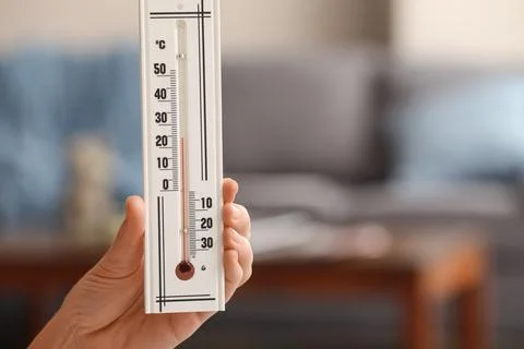 Hand holding a white thermometer with celsius scale, measuring room temperatu Stock Photos