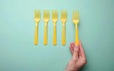 Hand holding yellow fork with four more yellow forks on blue background Stock Photos
