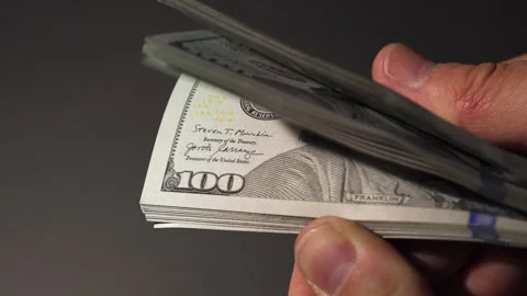 A hand holds and counts a stack of 100 dollar bills against a dark background Stock-Footage 314382308