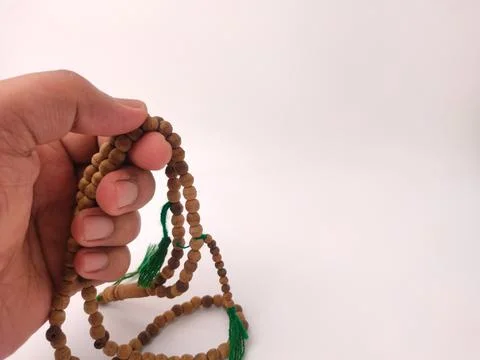 A hand holds and counts a string of brown wooden prayer beads against a whi.. Фото