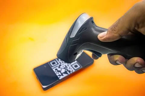 A hand holds a barcode scanner aimed at a smartphone displaying a QR code o.. Stock Photos